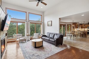 A spacious living area with a fireplace, a leather sofa, and a dining area with a kitchen in the background. - Heated Pool, Game Room & Outdoor Living Near Ha Ha Tonka (Camdenton)