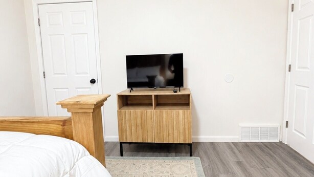 A bedroom with a bed, a TV on a wooden stand, a white door, and a patterned rug. - The Guernsey Getaway New Construction 3 Bedroom 2 Bathroom (Memphis)