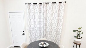A dining area with a round table, two chairs, a bowl of fruit, a potted plant, and a patterned curtain. - The Guernsey Getaway New Construction 3 Bedroom 2 Bathroom (Memphis)