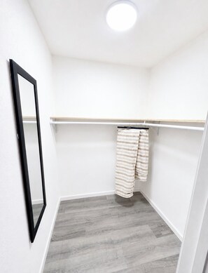 A small, well-lit room with a wooden floor, a mirror, and a clothing rack with striped garments. - The Guernsey Getaway New Construction 3 Bedroom 2 Bathroom (Memphis)