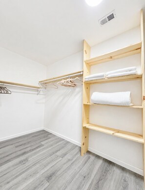 A room with a wooden shelf unit against the wall, a wooden floor, and a white ceiling with a vent. - The Guernsey Getaway New Construction 3 Bedroom 2 Bathroom (Memphis)
