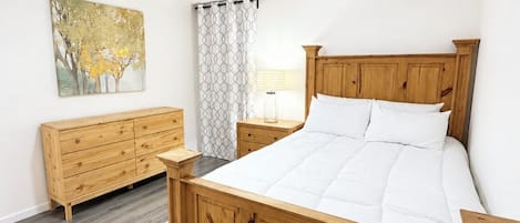 A bedroom with a wooden bed, a ceiling fan, a nightstand, a dresser, a patterned rug, and a painting on the wall.
