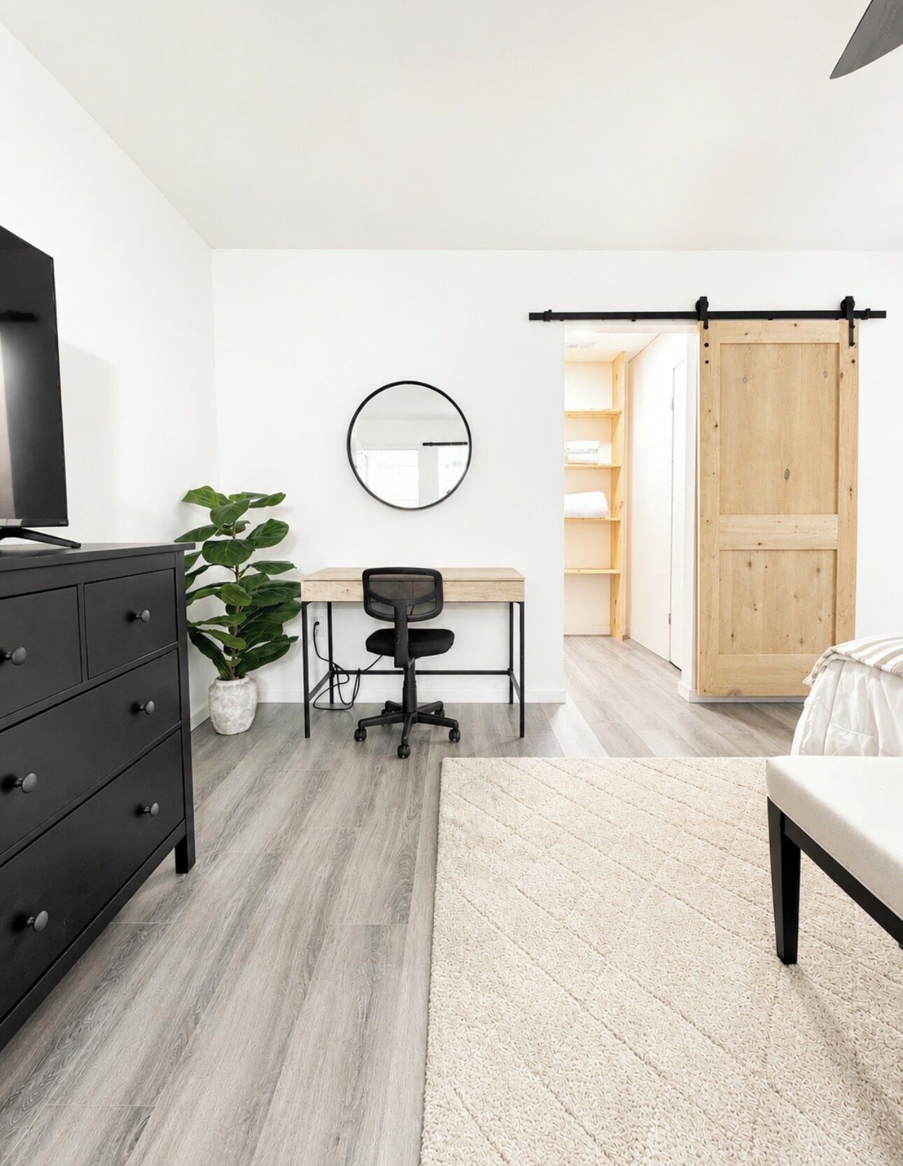 Ein modernes Schlafzimmer mit Bett, Schreibtisch, Stuhl, Kommode, Spiegel und einer Schiebetür.