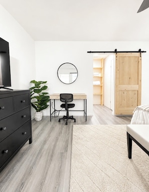 A modern bedroom with a bed, a desk, a chair, a dresser, a mirror, and a sliding door.