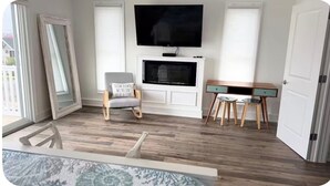 A room with a fireplace, a television mounted above it, a desk with two chairs, and a window with a view of the outside. - Spacious 5-bedroom house in peaceful Brigantine with AC (Brigantine)