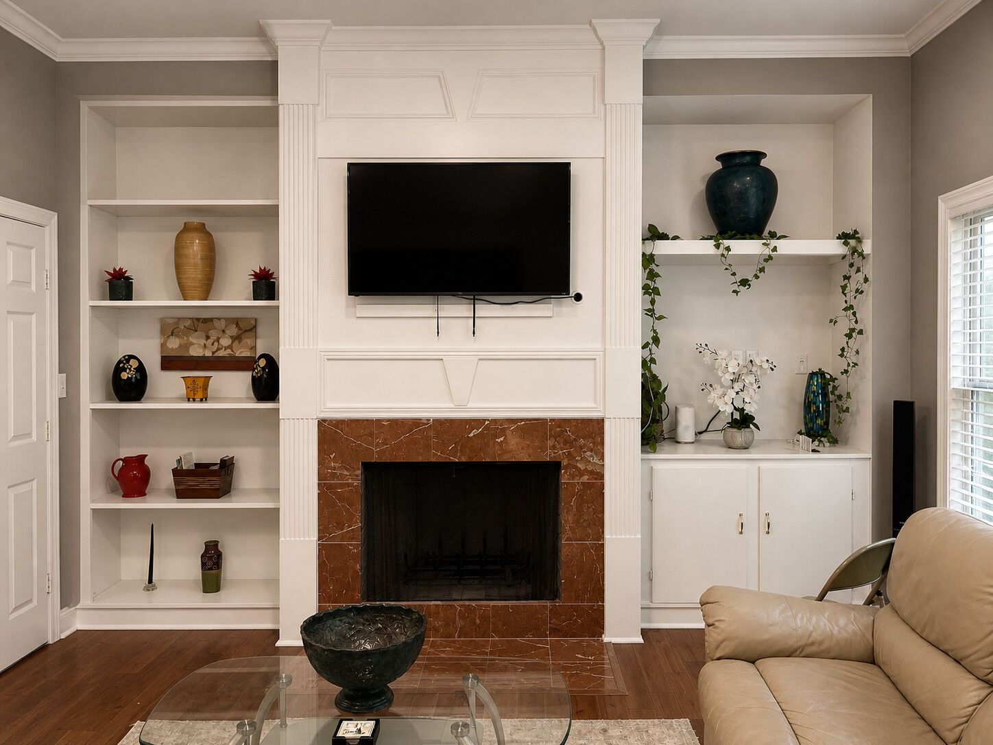 A living room with a fireplace, television, and various decorative items on shelves.