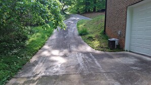 Ein Betonweg führt zu einer Garage mit einer Backsteinmauer und einer Klimaanlage.