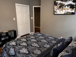 Een slaapkamer met een bed, een deur, een schilderij en een consoletafel.