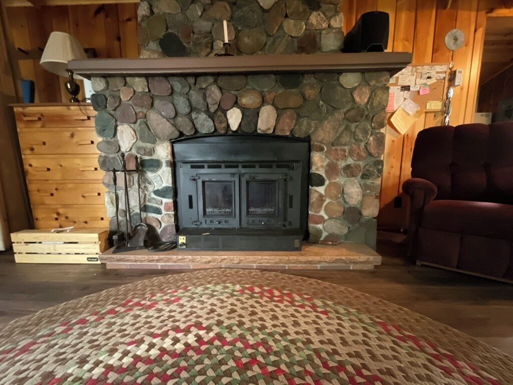 Une cheminée en pierre avec un manteau de cheminée, une commode en bois et un tapis à motifs.