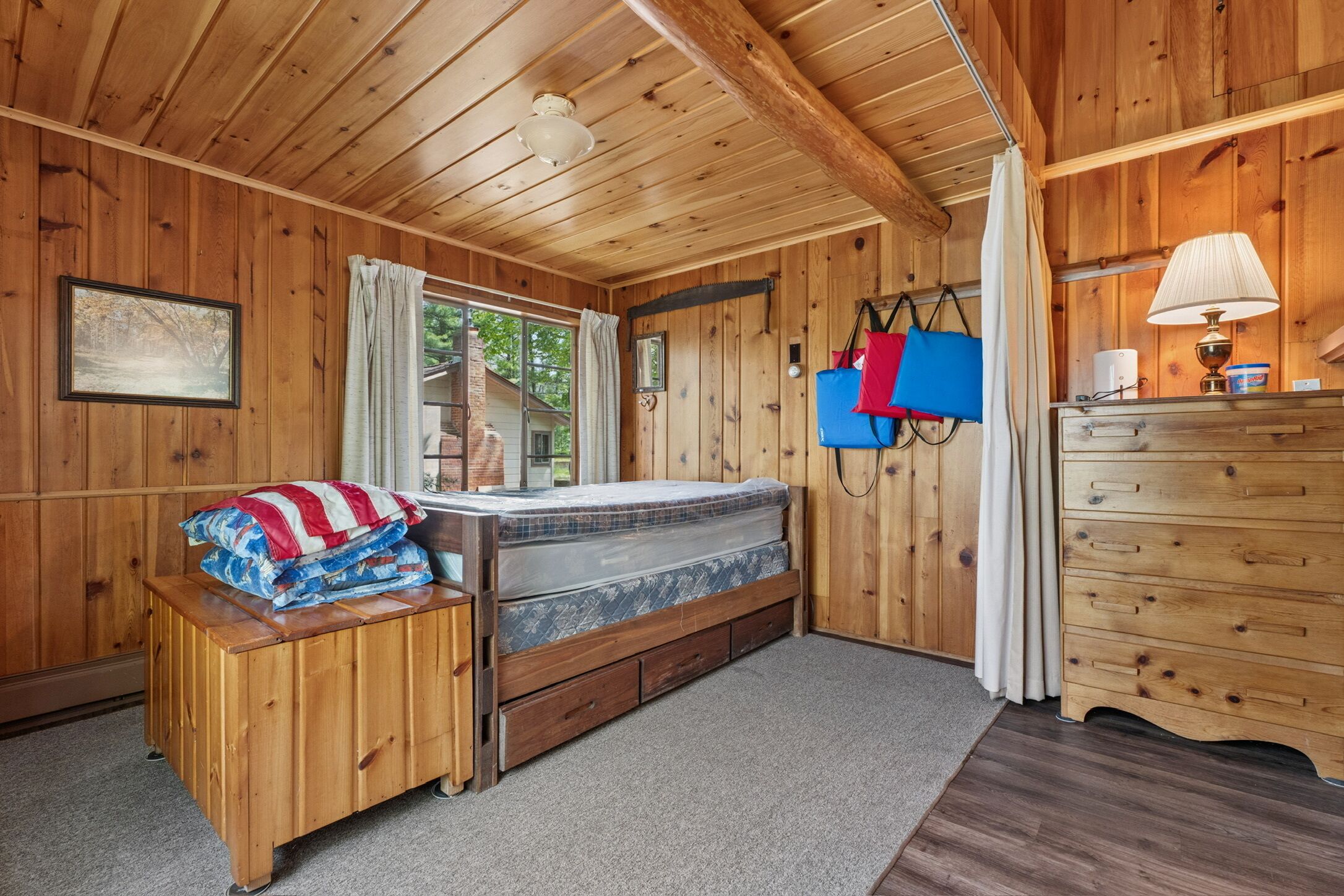 Une pièce de cabane en bois comprenant un lit, une commode, une fenêtre et une lampe.
