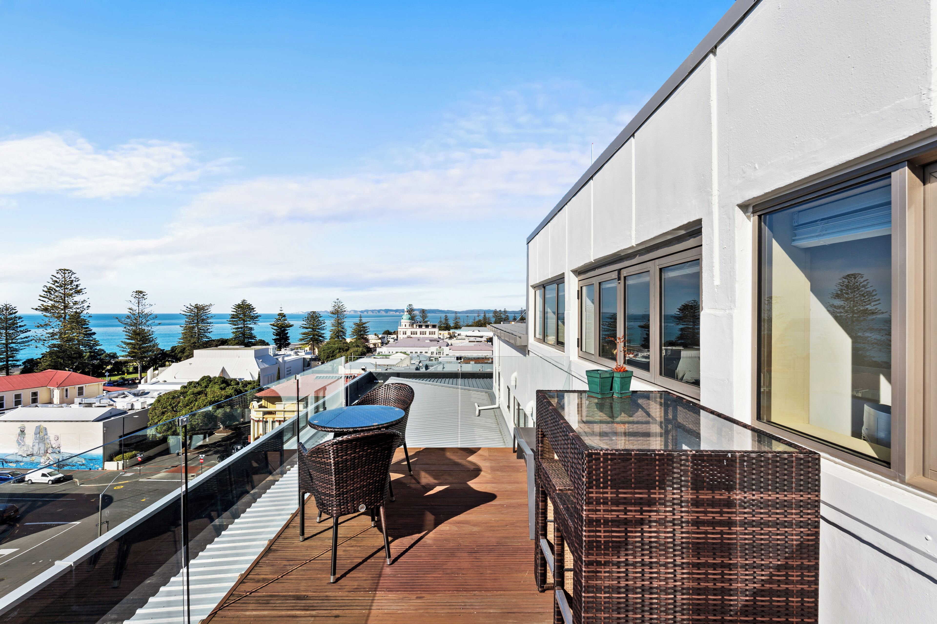 A balcony with a table and chairs, overlooking a cityscape and the sea.