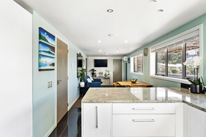A kitchen with white cabinets, a granite countertop, a dining area with a table and chairs, and a window with blinds. - Sea and City Penthouse - Napier CBD (Napier)