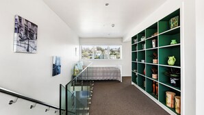 Un interno moderno con una scala, un letto, una scaffalatura verde e opere d'arte alle pareti.