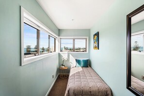 A bedroom with a bed, a window, a small table with a plant, and a painting on the wall. - Sea and City Penthouse - Napier CBD (Napier)
