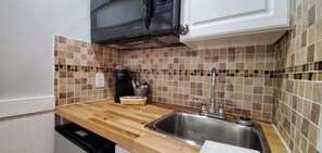 A kitchen with a microwave, sink, and tiled backsplash. - Bright Rodeo Retreat | Walk to Everything 246 (River Ranch)