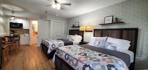 A bedroom with two beds, a desk, and a kitchenette. - Bright Rodeo Retreat | Walk to Everything 246 (River Ranch)