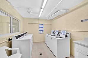 Een wasserette met meerdere wasmachines en drogers, een plafondventilator en een raam.