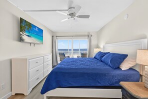 A bedroom with a bed, a ceiling fan, a window with curtains, a nightstand, and a wall-mounted TV displaying a beach scene. - Sugar Sand Beachfront Condo, Spectacular Gulf Views, 24' Lanai, 2BR/2BA, #433 (Fort Myers Beach)