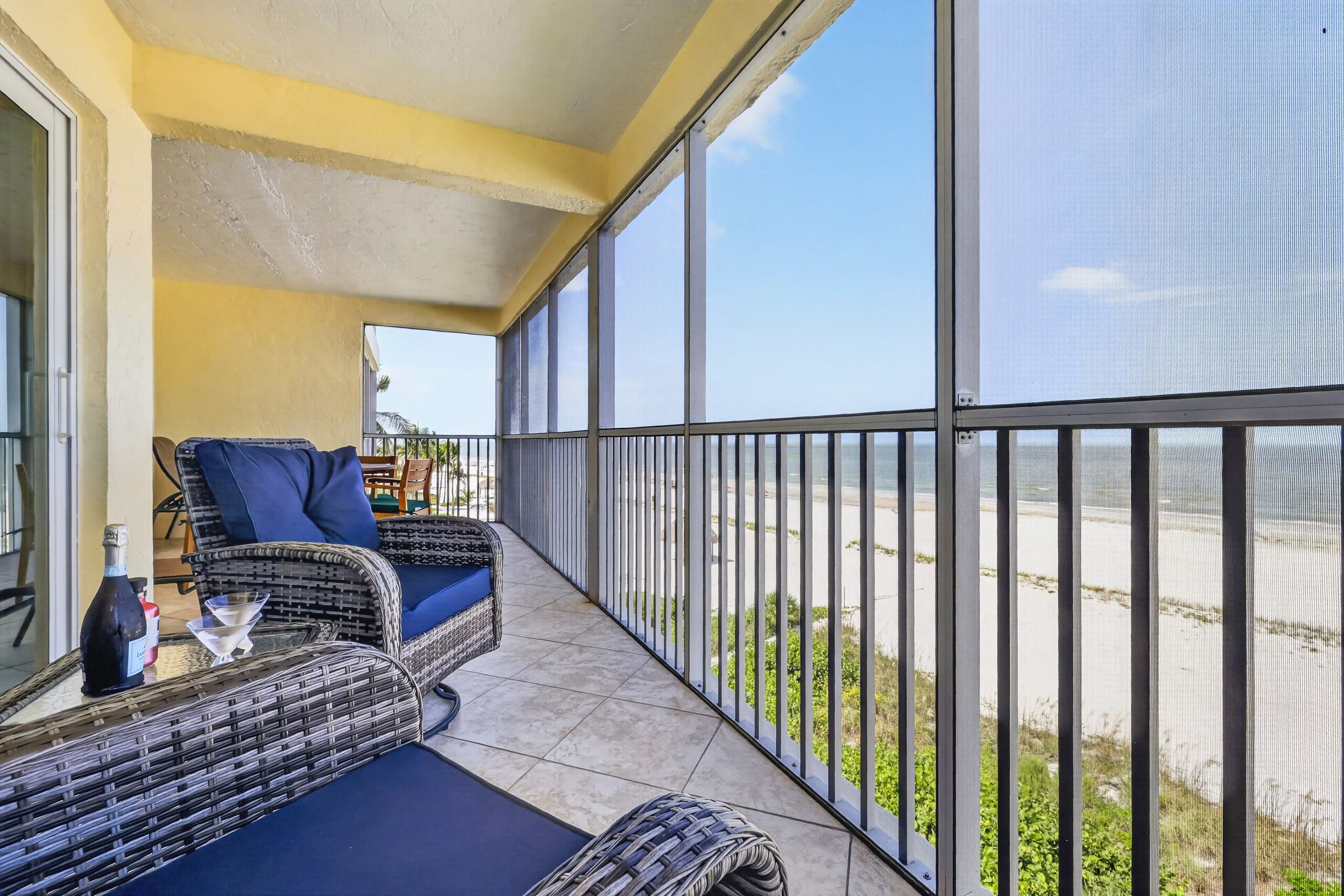 A balcony with wicker furniture, a glass table, and a view of the beach.