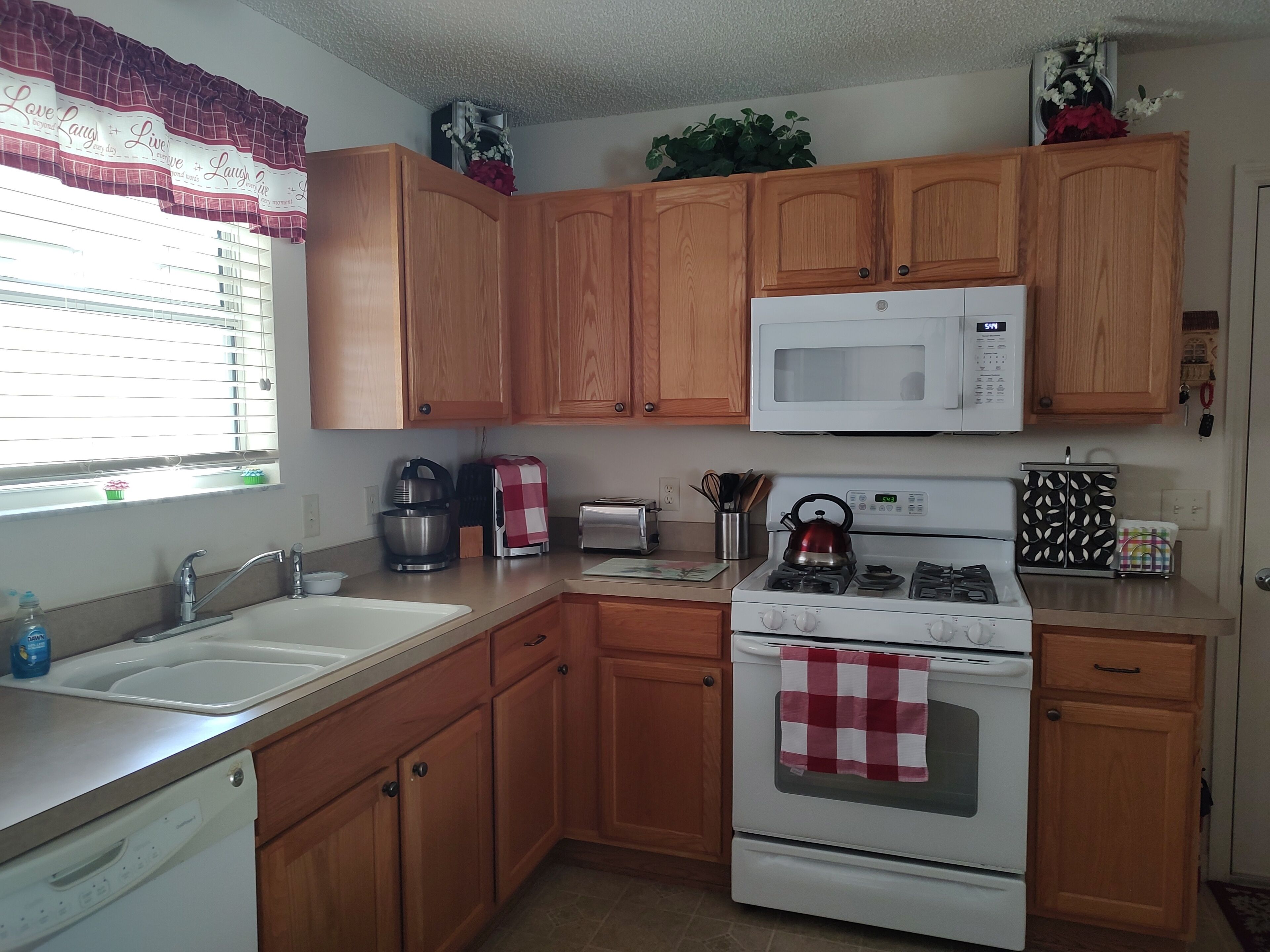 A kitchen with wooden cabinets, a microwave, a stove, a sink, and a window with blinds.