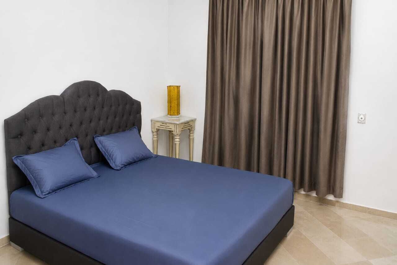 A bed with a tufted headboard, two pillows, and a blue bedspread.