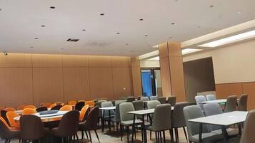 A conference room with multiple tables and chairs, a high ceiling with recessed lighting, and a neutral color scheme.