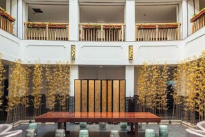 A spacious lobby with a central wooden table, surrounded by seating, and a decorative bamboo arrangement.