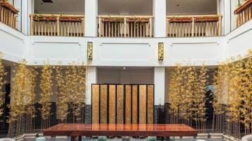A spacious lobby with a central wooden table, surrounded by seating, and a decorative bamboo installation.