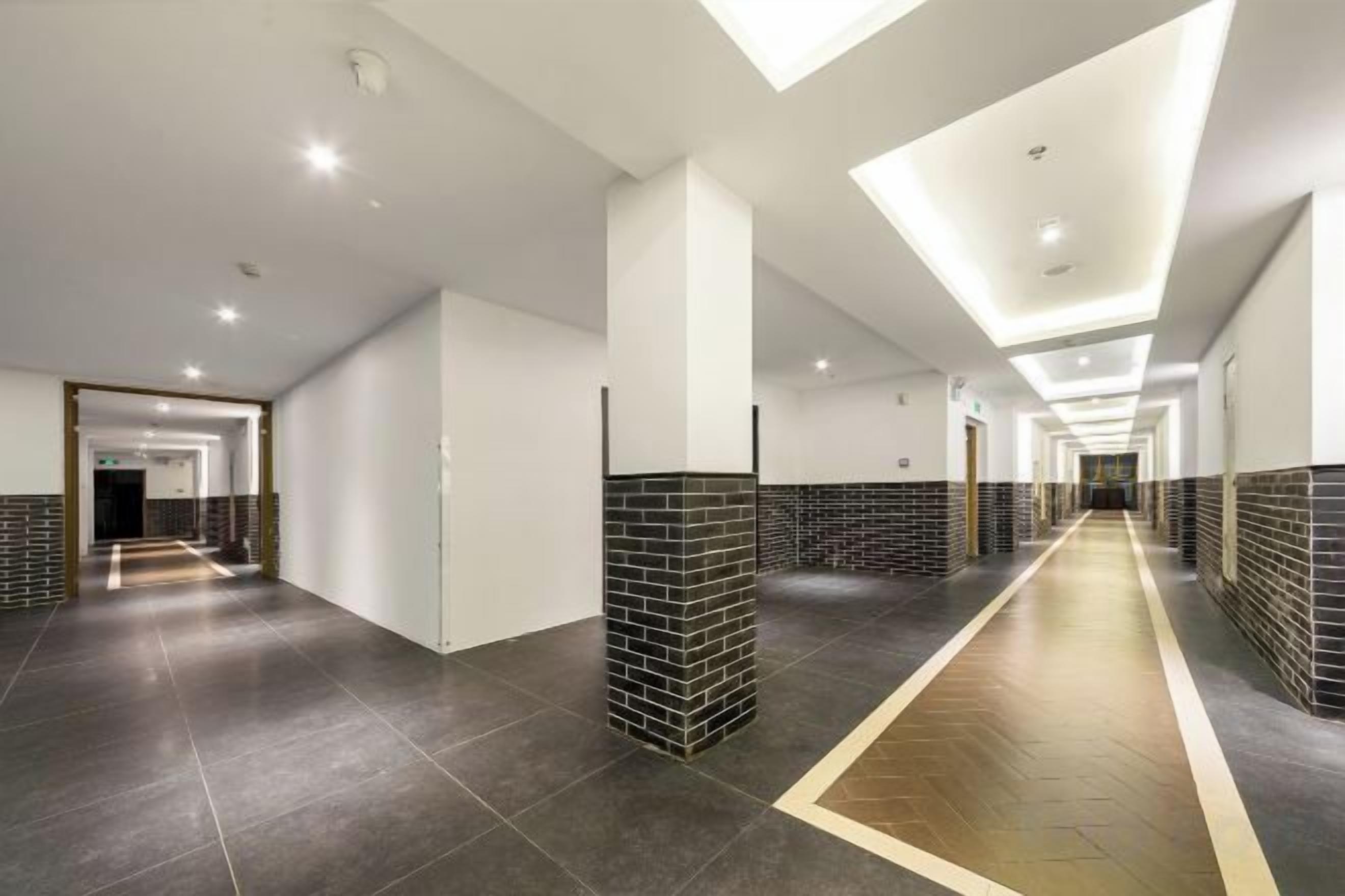 A long corridor with tiled walls and a central walkway, leading to multiple doors.