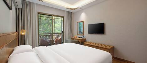 A hotel room with a large bed, a desk, a TV, and a balcony with a view of greenery.