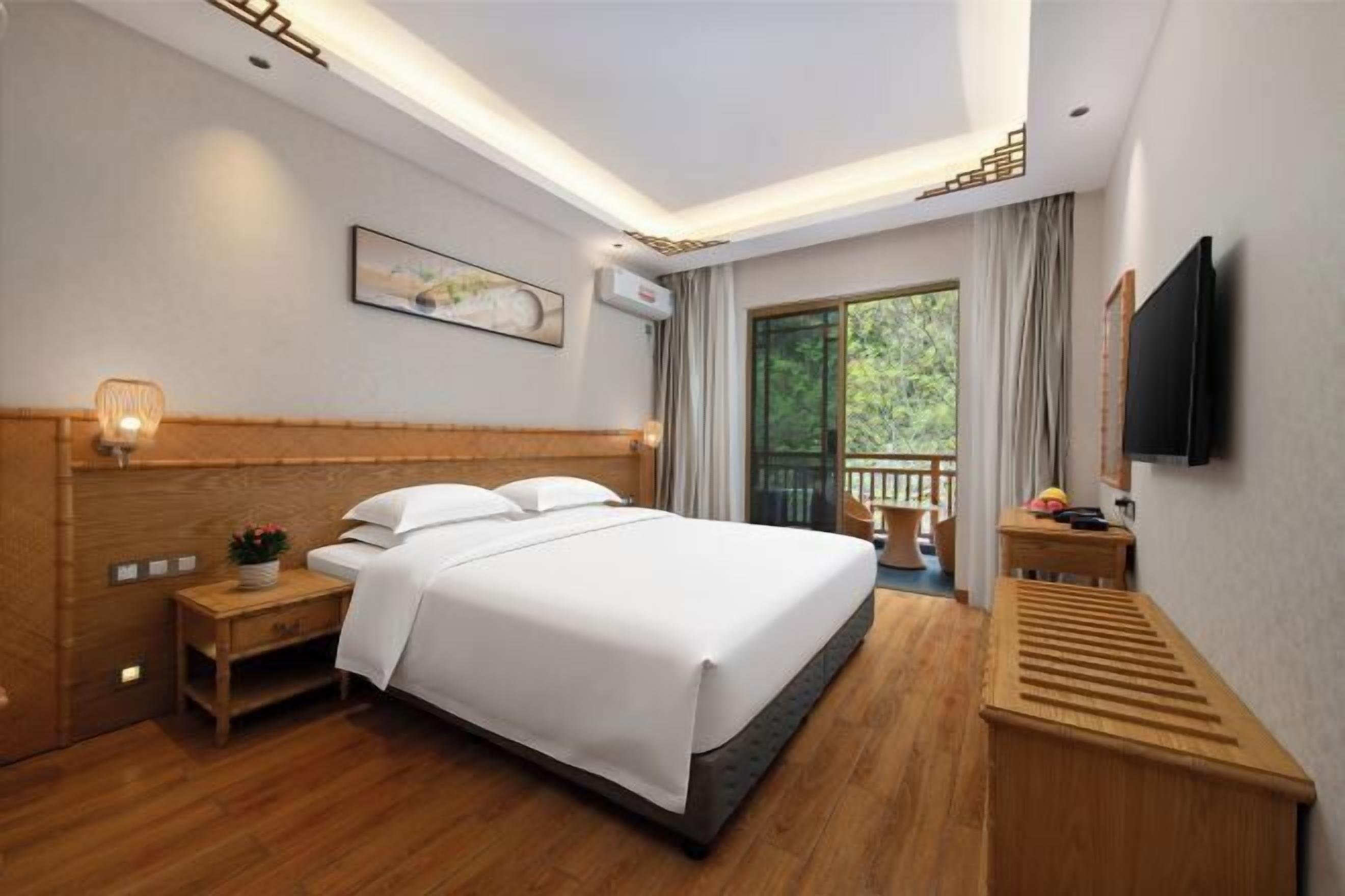 Habitación de hotel con una cama grande, mesita de noche y televisor montado en la pared.