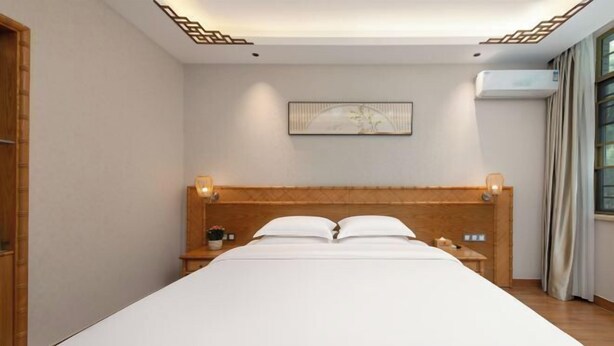 A hotel room with a large bed, wooden headboard, bedside tables, and a wall-mounted air conditioner. - Libo Daqikong Bamboo Garden Boutique Hotel (East Gate Ticket Hall Store of Xiaoqikong Scenic Area) (Libo)