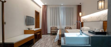 A hotel room with a bed, a desk, a chair, a TV, a bathroom with a sink and mirror, and a window with curtains.
