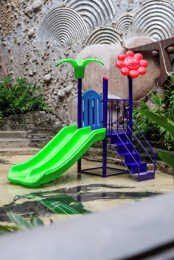 A playground with a green slide, a blue climbing structure, and a red flower decoration.