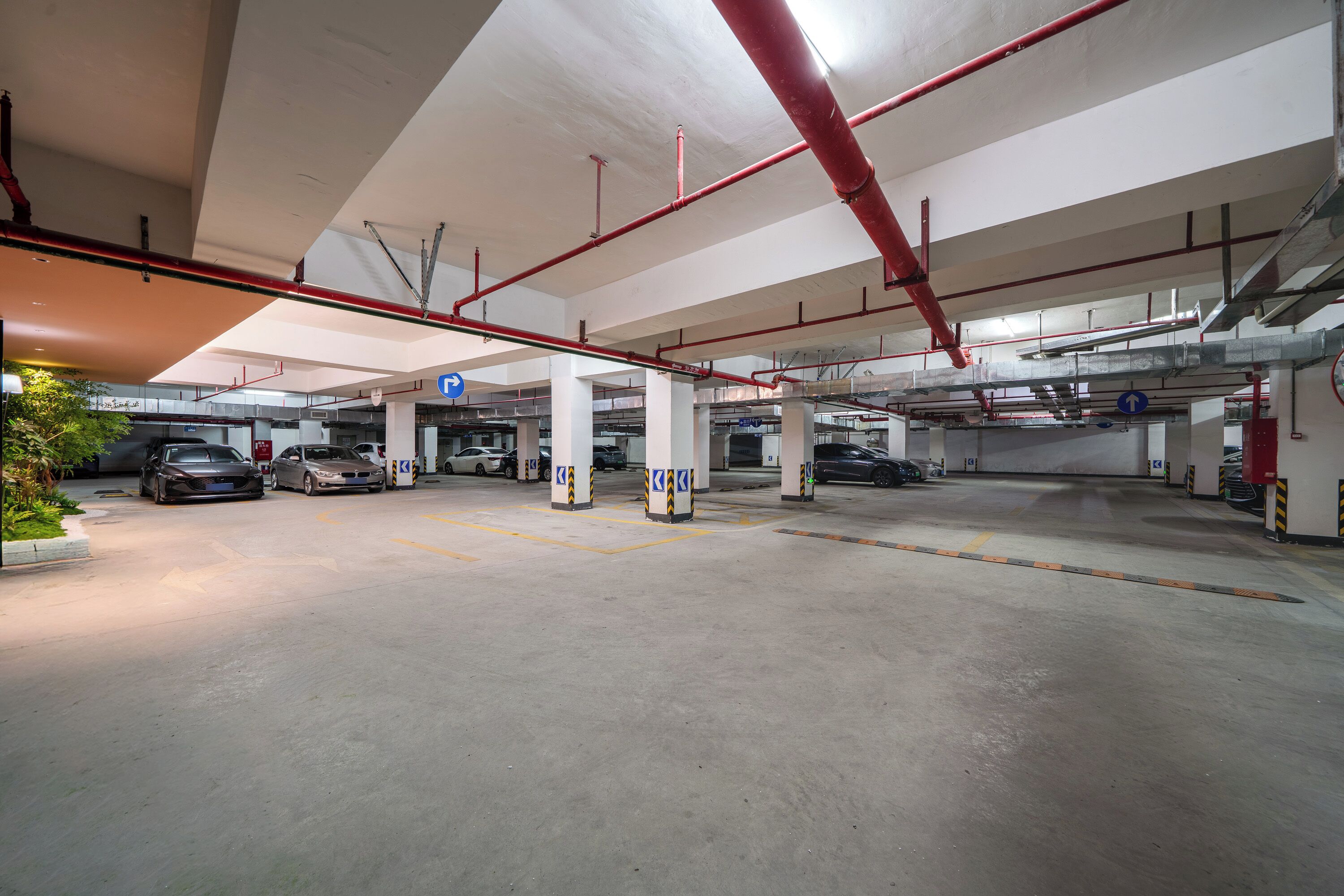 Un estacionamiento subterráneo con varios niveles, pilares de hormigón y señalización direccional.