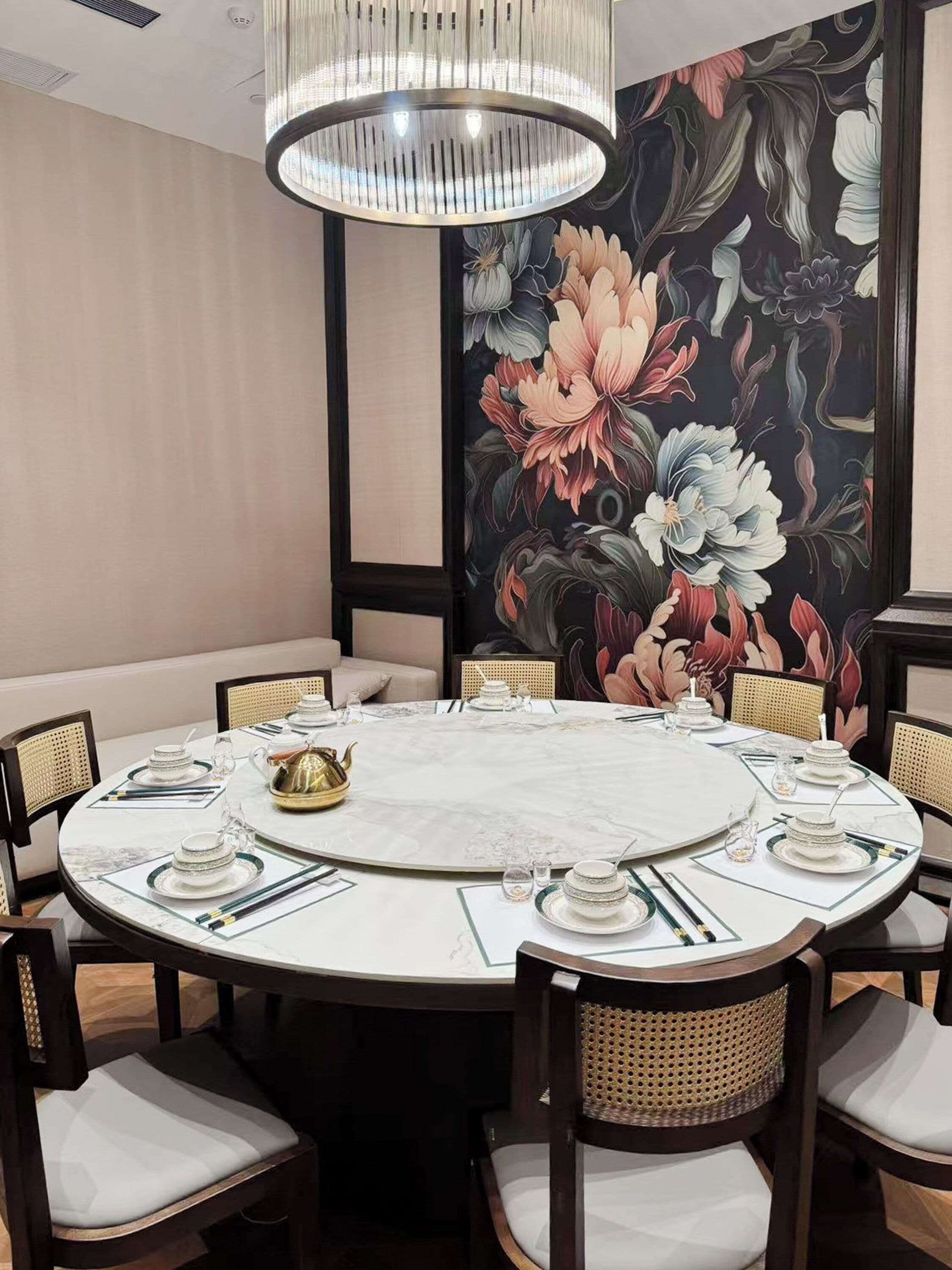 A round dining table with white marble top, surrounded by wooden chairs with woven seats, set with fine china and glassware.