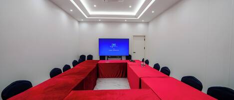 Uma sala de conferências com uma mesa comprida, cadeiras, uma tela de projetor e uma porta.