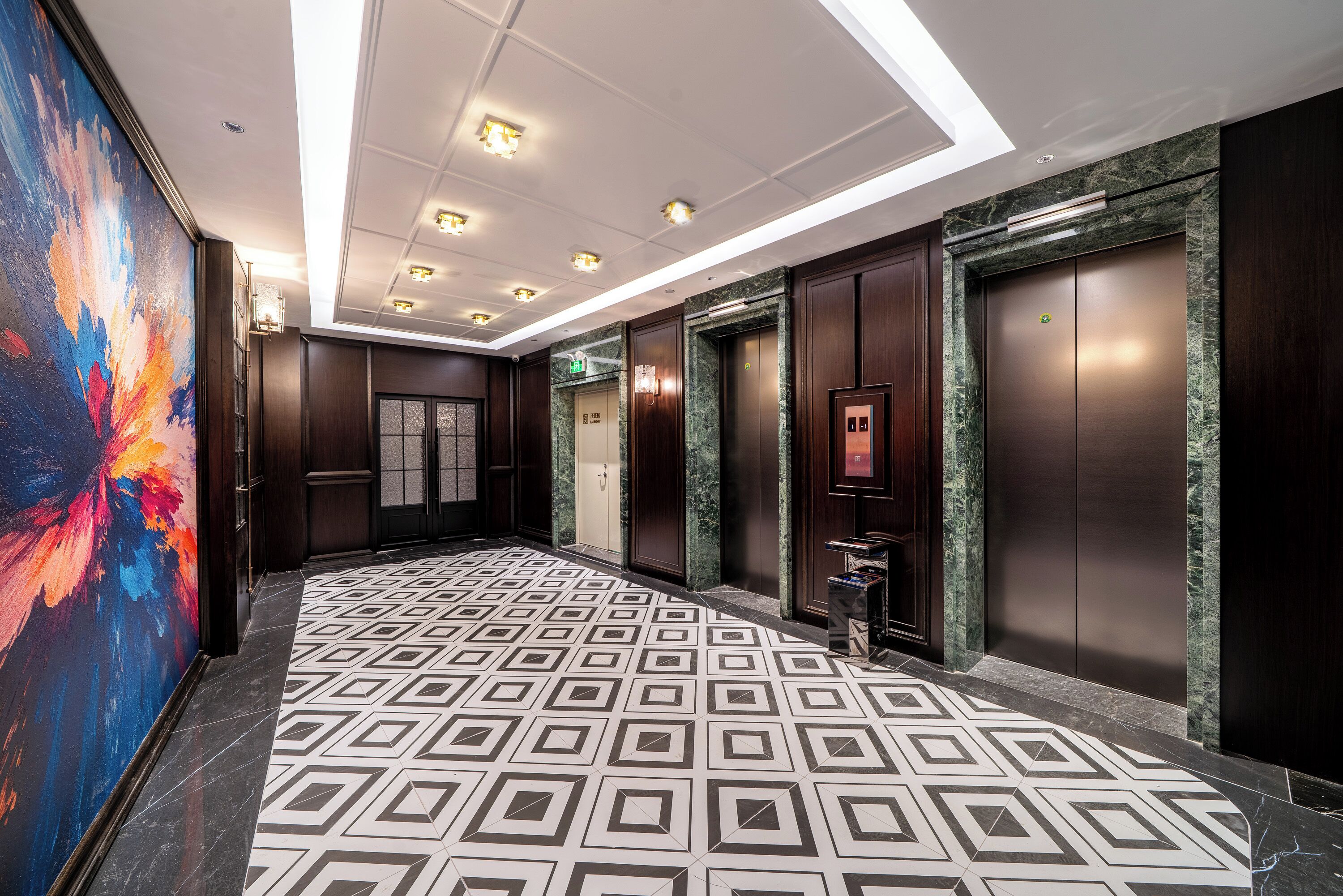 A hotel lobby with a geometric patterned floor, dark wood paneling, and a colorful abstract painting on the left.