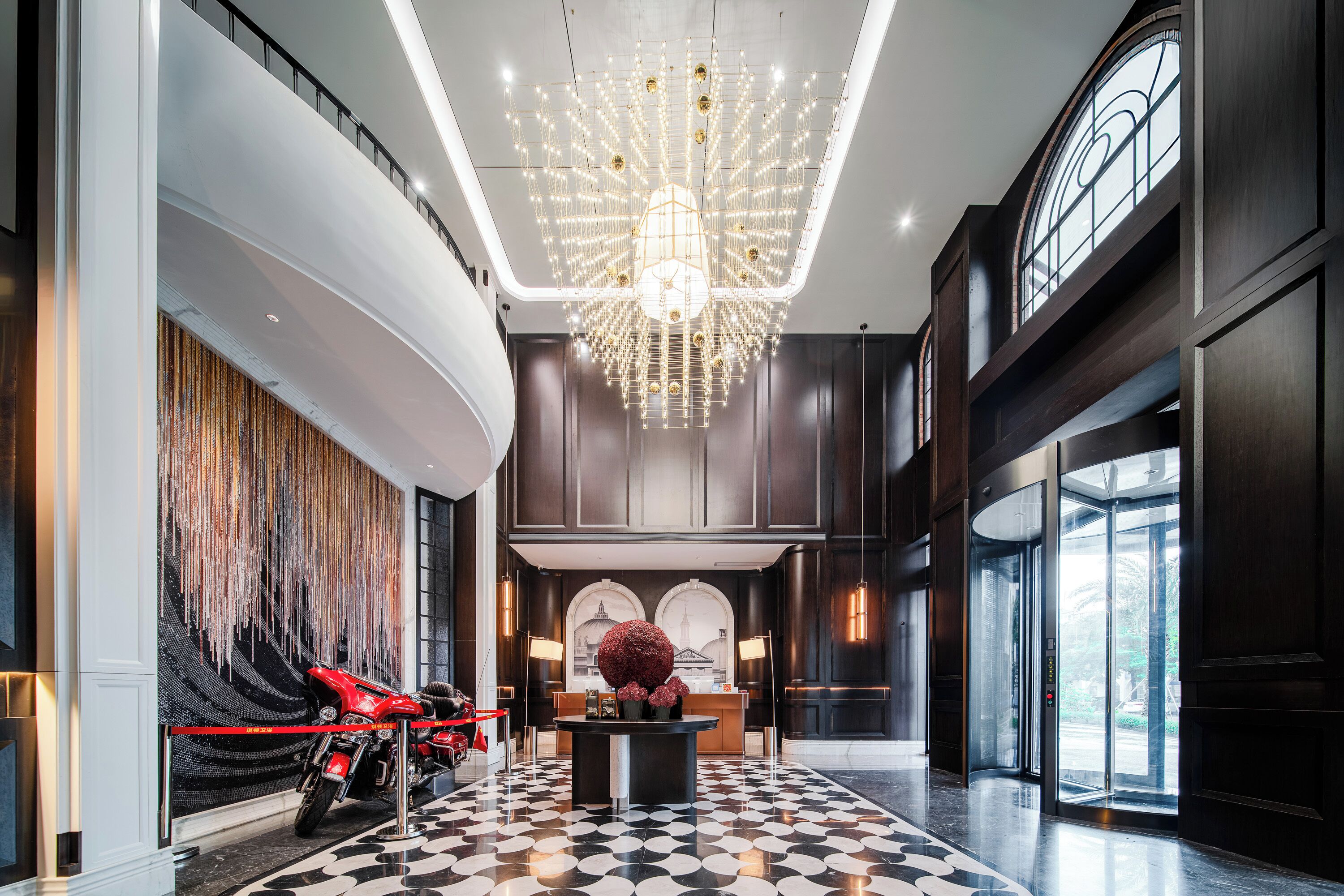 A spacious lobby with a large chandelier, a reception desk, and a motorcycle display.