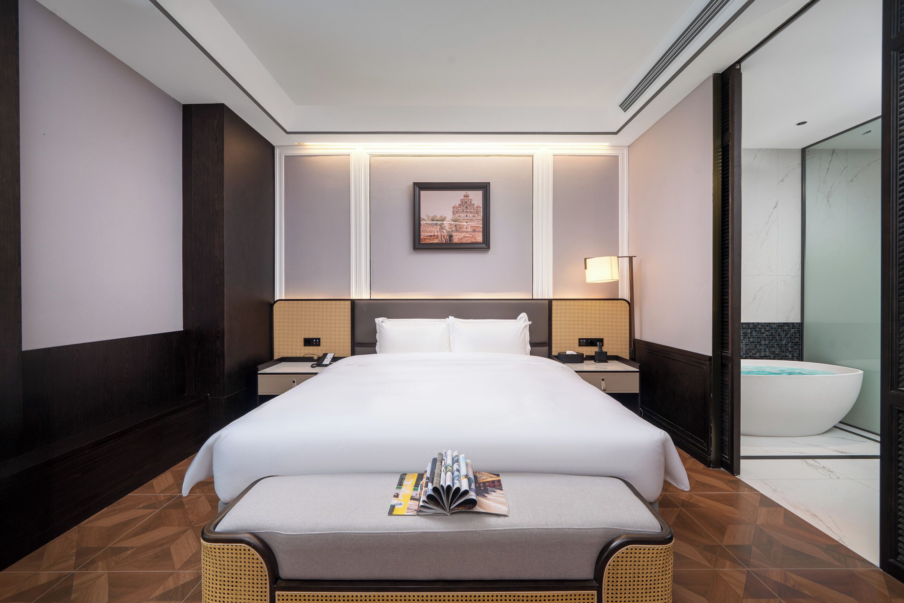 Habitación de hotel con una cama grande, una mesita de noche, una lámpara de noche, un cuadro colgado en la pared, un baño con bañera y un espejo grande.