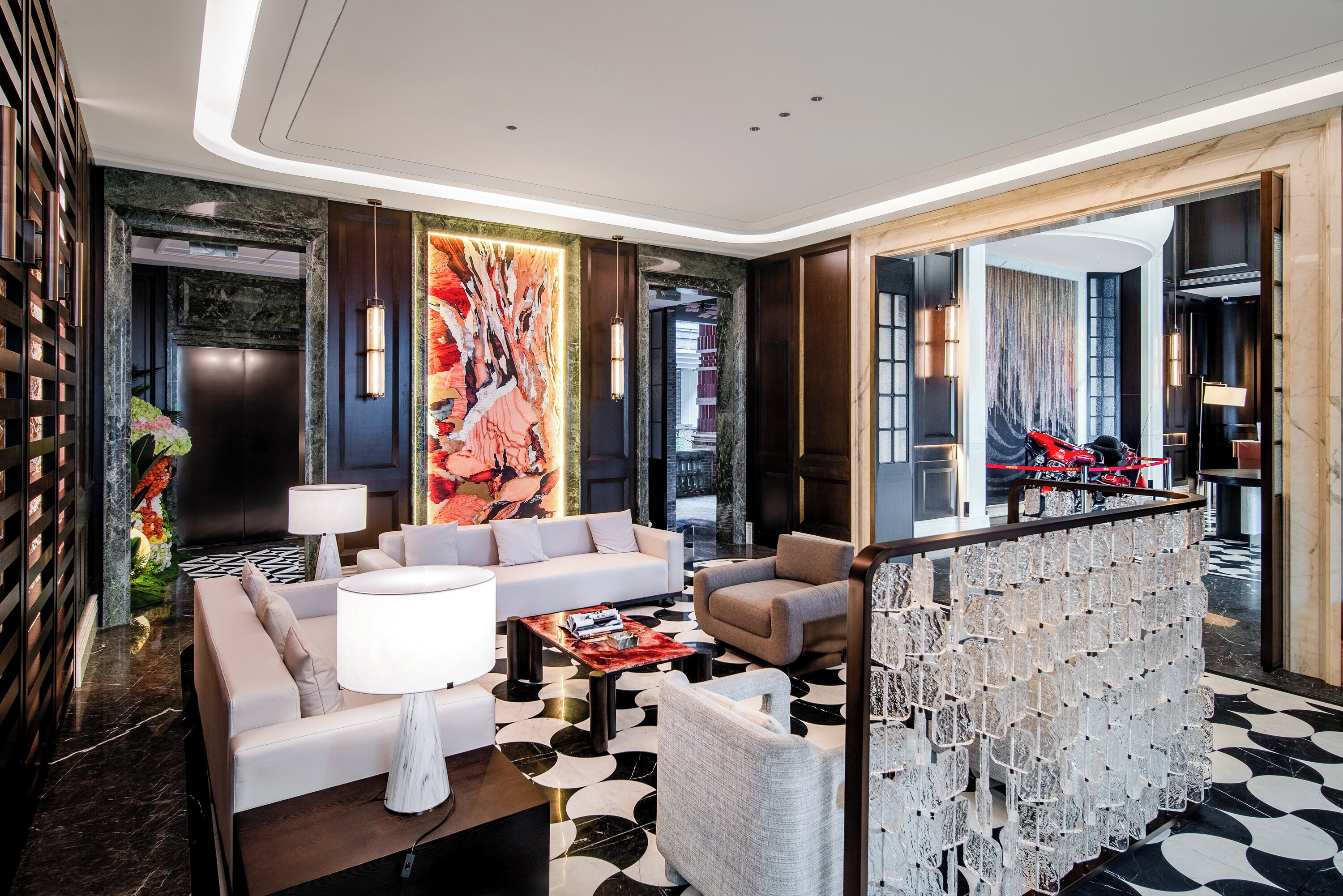 Um hall de hotel moderno com sofá, poltronas, mesa de centro, um espelho grande e um detalhe decorativo na parede.