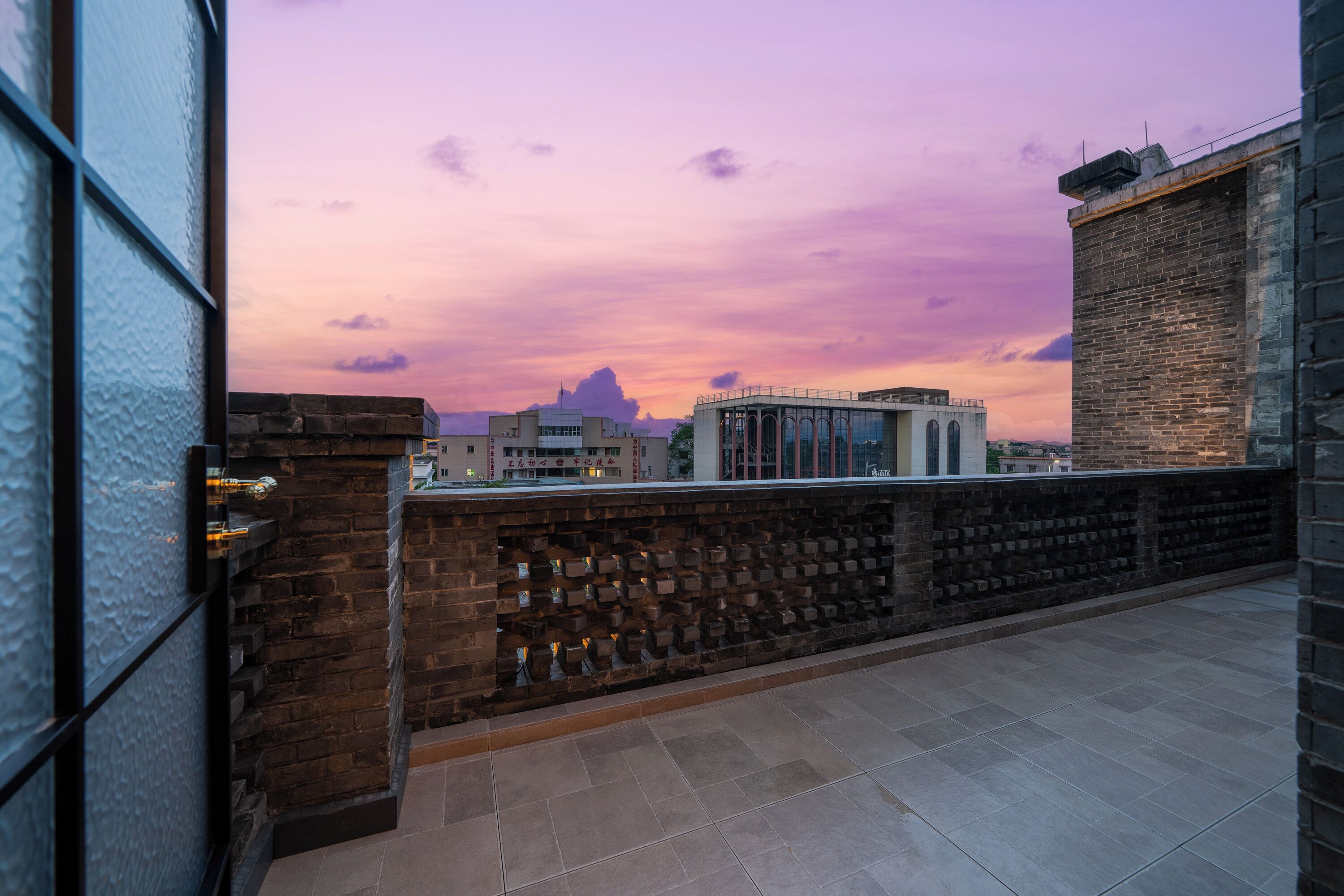 A rooftop terrace with a brick wall and a view of the city skyline at sunset.