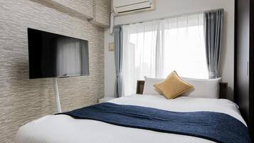 Habitació d'hotel amb un llit, un televisor de pantalla plana al mur, una finestra amb cortines i un aparell d'aire condicionat.