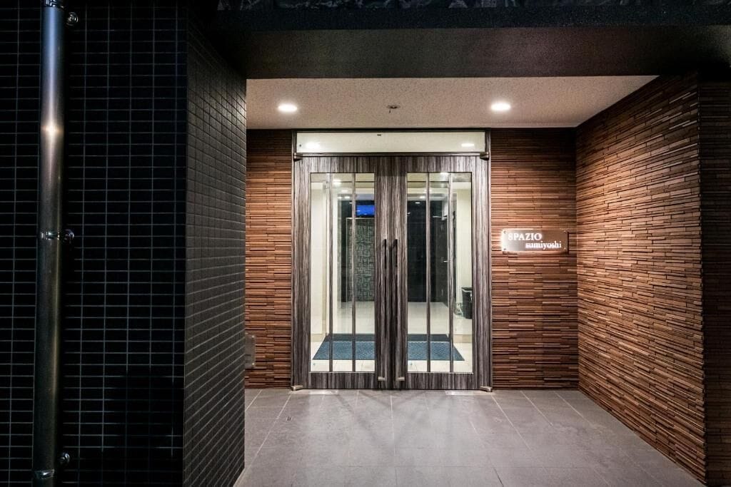 Entrada de un edificio moderno con puerta de vidrio, un letrero que dice 'SPAZIO' y piso de baldosas.