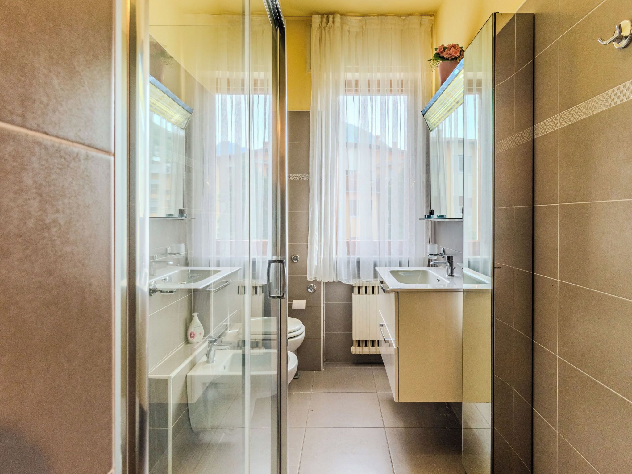 Un baño con cabina de ducha de vidrio, dos lavamanos, un inodoro y un espejo sobre el lavamanos.