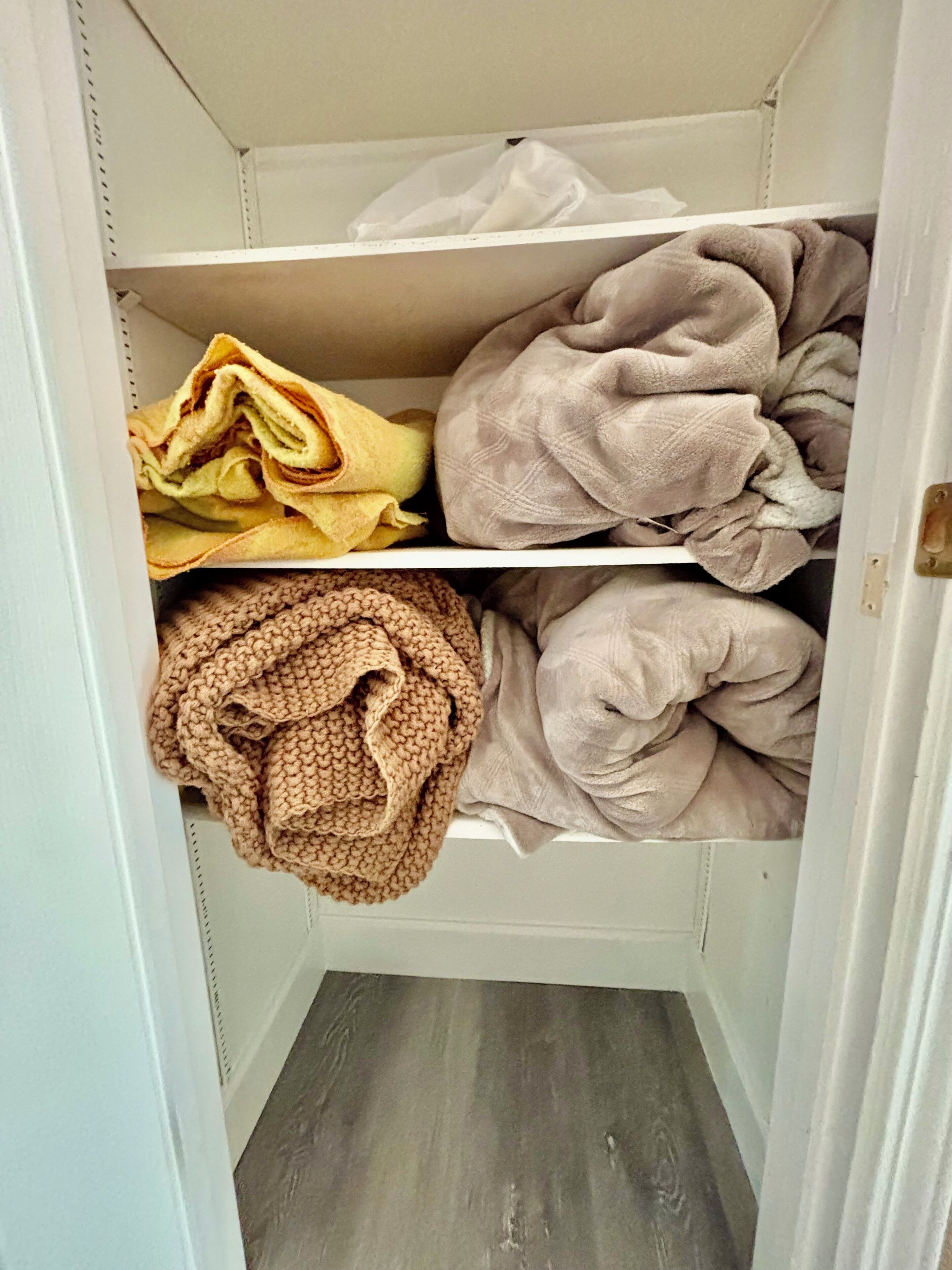A closet with shelves containing folded blankets and a knitted item.