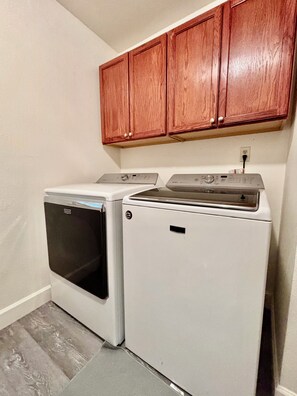 A laundry area with a front-loading washer and dryer, wooden cabinets above, and a gray floor. - Spacious 5BR Pet-Friendly Retreat on a 14,000 Sq Ft Lot (Stockton)