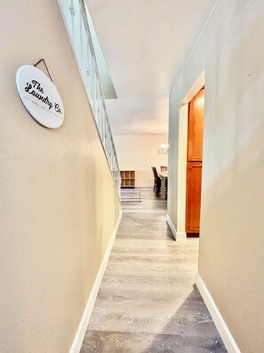 A hallway with a wooden floor, a staircase on the left, and a door on the right. - Spacious 5BR Pet-Friendly Retreat on a 14,000 Sq Ft Lot (Stockton)