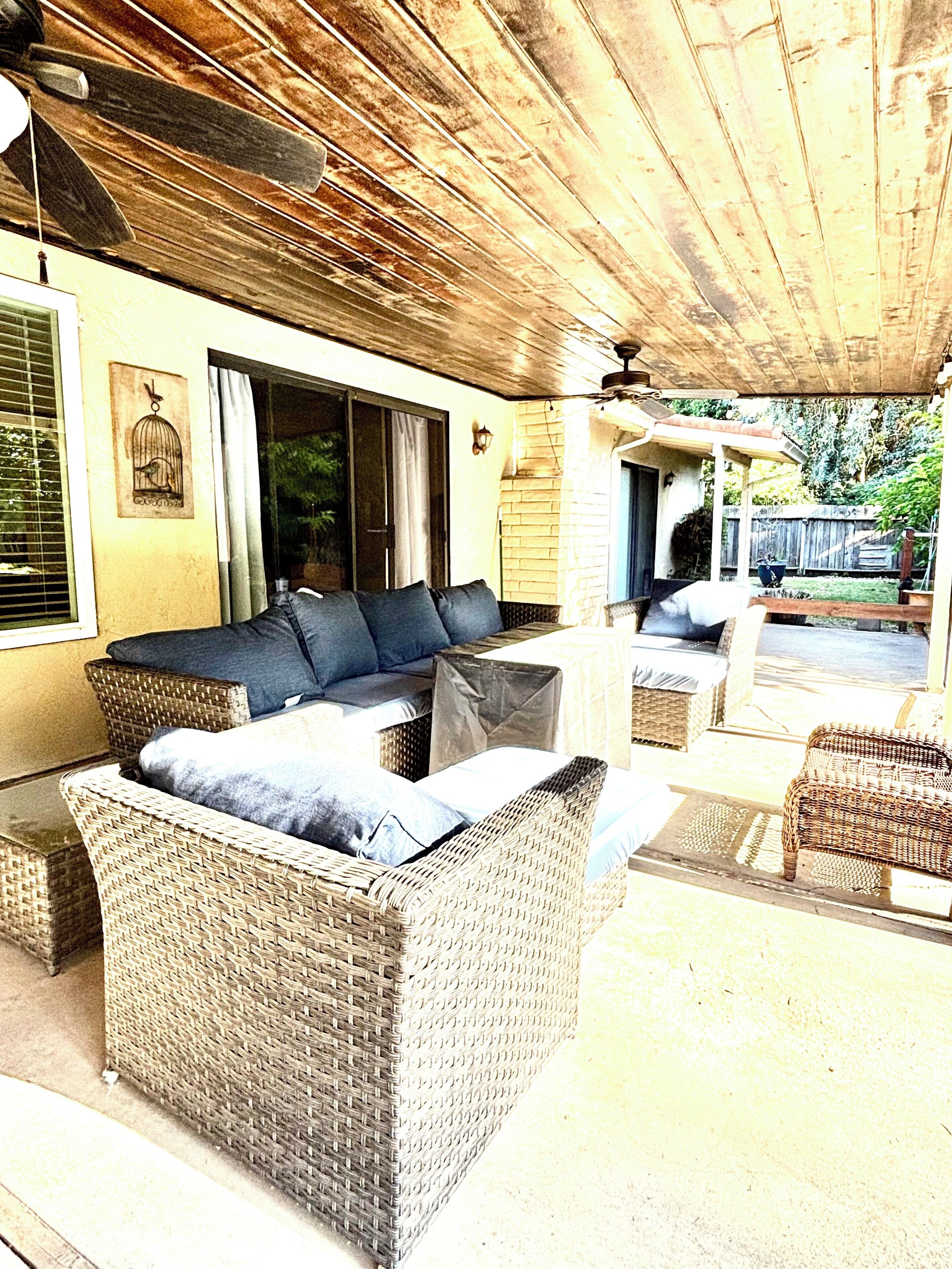 An outdoor seating area with wicker furniture, a ceiling fan, and a view of the backyard.