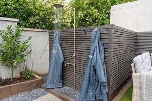 Een overdekt buitengebied met een douche, een bank en een aan de muur bevestigde handdoekhouder.